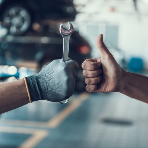 Close-up Thumb Up and Mechanics Hand with Tool. Automobile Master Wearing Gloves Showing Positive Gesture after Finishing Work. Technic occupation. Automobile Repair Service Concept.