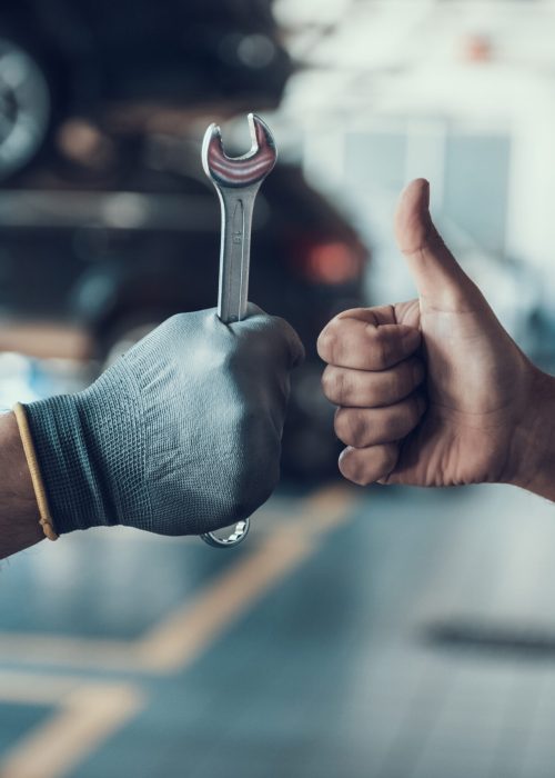 Close-up Thumb Up and Mechanics Hand with Tool. Automobile Master Wearing Gloves Showing Positive Gesture after Finishing Work. Technic occupation. Automobile Repair Service Concept.