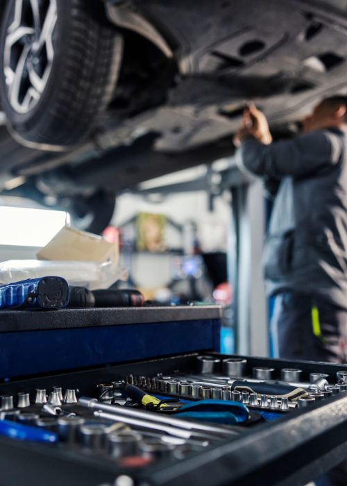 Close up of a tools in a drawer on toolbox with worker repairing car in blurry background at mechanic's shop.